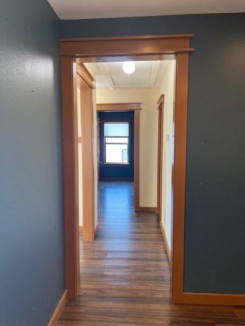 hall with dark wood-style flooring, attic access, and baseboards