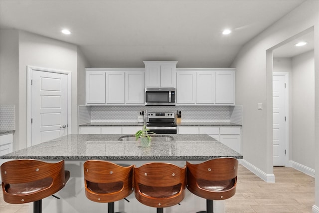 kitchen featuring white cabinetry, decorative backsplash, an island with sink, and appliances with stainless steel finishes