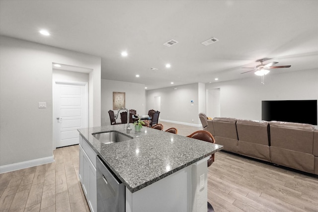 kitchen featuring stone counters, white cabinetry, sink, stainless steel dishwasher, and a center island with sink