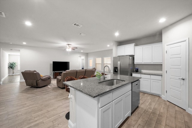 kitchen with stone counters, a center island with sink, sink, white cabinetry, and stainless steel appliances