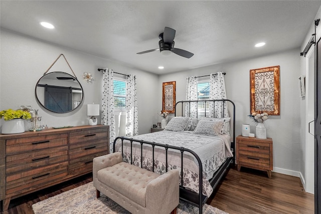 bedroom with dark wood-type flooring, ceiling fan, a barn door, and multiple windows