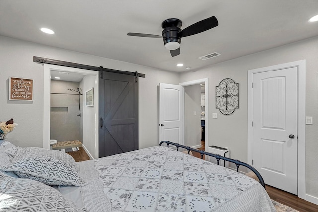 bedroom featuring ceiling fan, dark wood-type flooring, ensuite bath, and a barn door