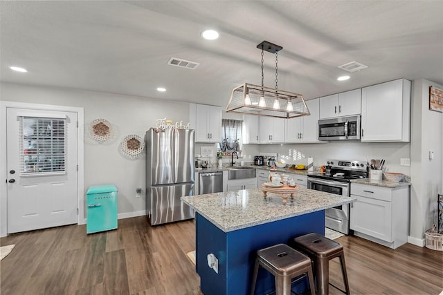 kitchen with appliances with stainless steel finishes, white cabinetry, a kitchen island, and decorative light fixtures