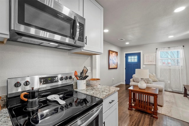 kitchen with dark wood-type flooring, stainless steel appliances, white cabinets, and light stone counters