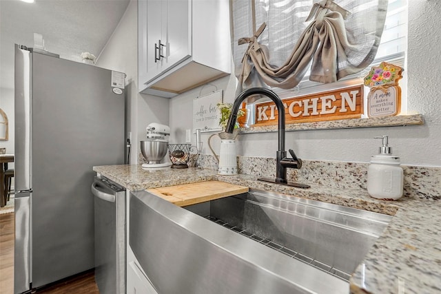 kitchen with white cabinets, stainless steel fridge, sink, and light stone counters