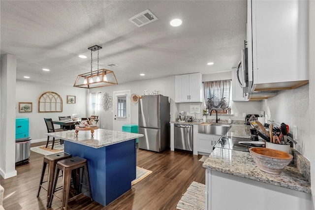 kitchen with pendant lighting, a kitchen island, dark wood-type flooring, stainless steel appliances, and white cabinets