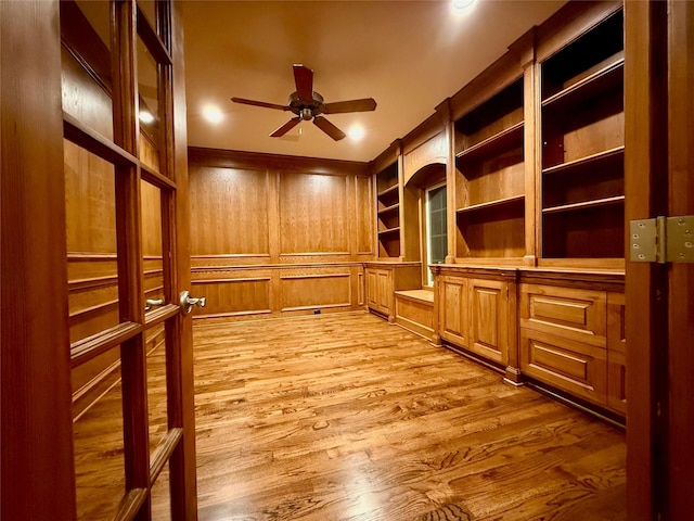 unfurnished office featuring light wood-type flooring, ceiling fan, wooden walls, and built in shelves