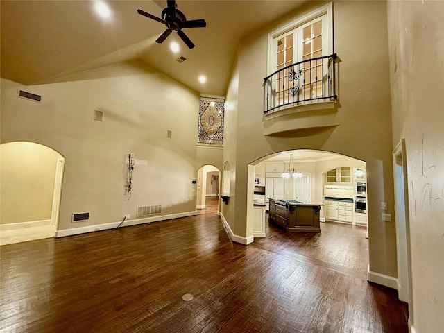 unfurnished living room with dark hardwood / wood-style flooring, ceiling fan with notable chandelier, and high vaulted ceiling