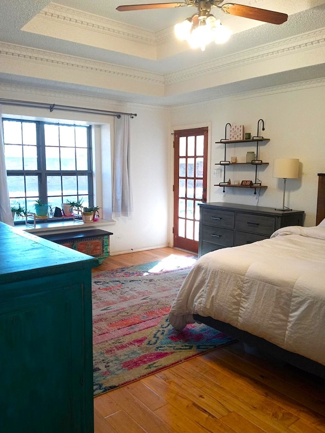 bedroom featuring crown molding, hardwood / wood-style floors, a textured ceiling, a raised ceiling, and ceiling fan