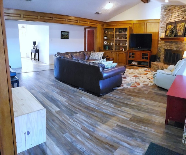 living room featuring built in shelves, a brick fireplace, vaulted ceiling with beams, and dark wood-type flooring