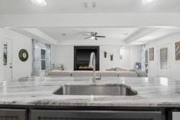 kitchen featuring a raised ceiling, light stone countertops, sink, and ceiling fan