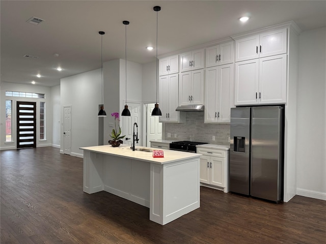 kitchen featuring white cabinetry, sink, stainless steel fridge, hanging light fixtures, and a kitchen island with sink