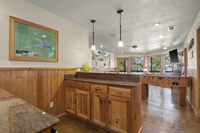 kitchen featuring kitchen peninsula, dark stone counters, a textured ceiling, hanging light fixtures, and wood walls