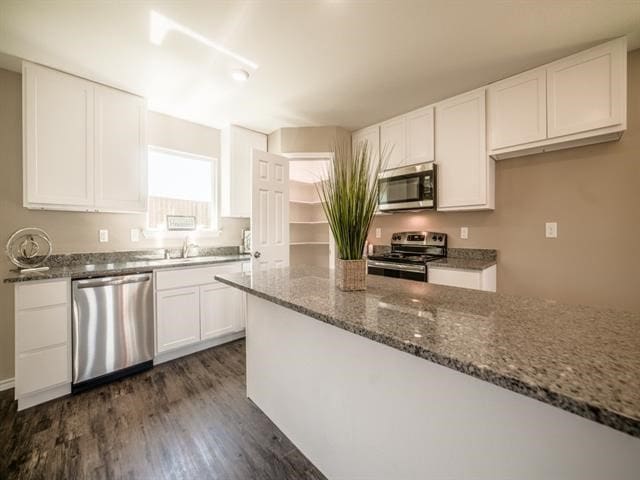 kitchen featuring sink, stainless steel appliances, dark hardwood / wood-style floors, dark stone countertops, and white cabinets