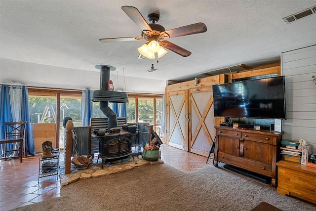 tiled living room with ceiling fan, wood walls, a wood stove, and a textured ceiling