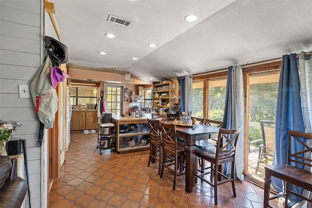 dining area featuring a textured ceiling, wooden walls, and lofted ceiling