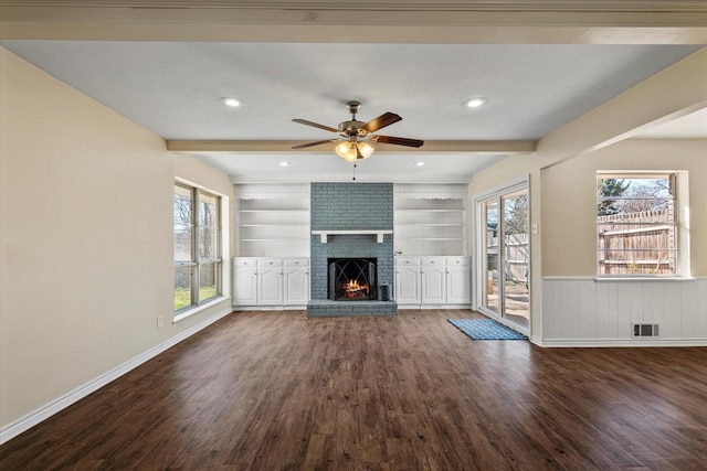 unfurnished living room featuring dark hardwood / wood-style flooring, built in features, beamed ceiling, and a brick fireplace