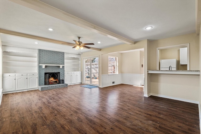 unfurnished living room with a brick fireplace, ceiling fan, built in features, beamed ceiling, and dark hardwood / wood-style flooring