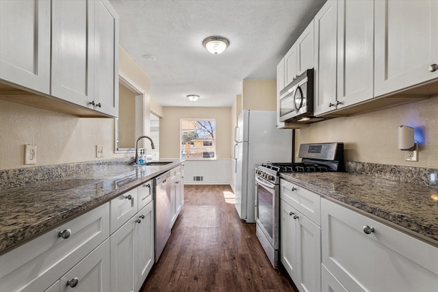 kitchen featuring dark stone counters, sink, dark hardwood / wood-style floors, appliances with stainless steel finishes, and white cabinetry