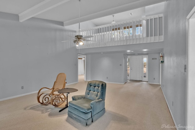 sitting room with a high ceiling, beam ceiling, ceiling fan, and light carpet