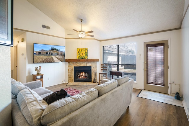 living room featuring a stone fireplace, vaulted ceiling, wood-type flooring, ceiling fan, and a textured ceiling