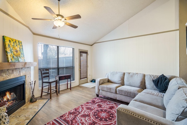 living room featuring a tile fireplace, light hardwood / wood-style floors, ceiling fan, a textured ceiling, and lofted ceiling