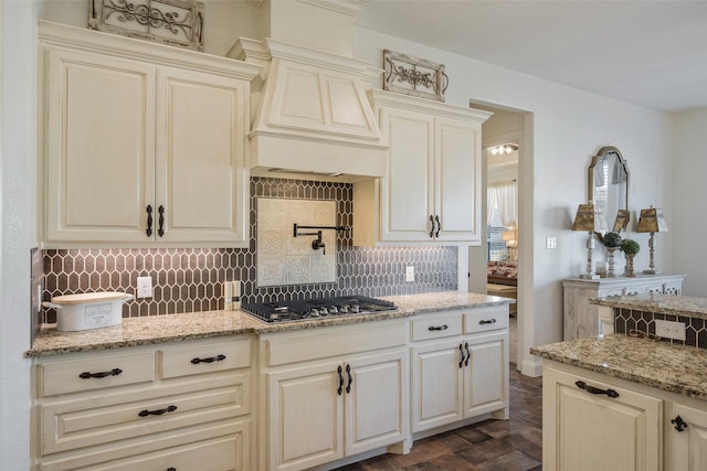 kitchen featuring decorative backsplash, light stone counters, custom range hood, and stainless steel gas cooktop