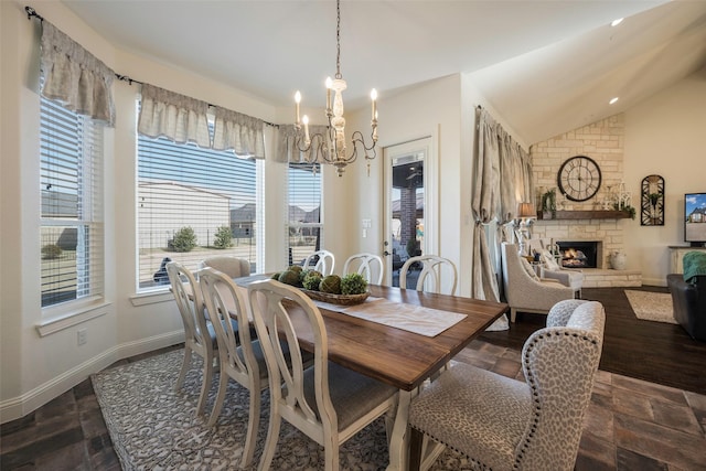 dining area with vaulted ceiling, an inviting chandelier, and a stone fireplace