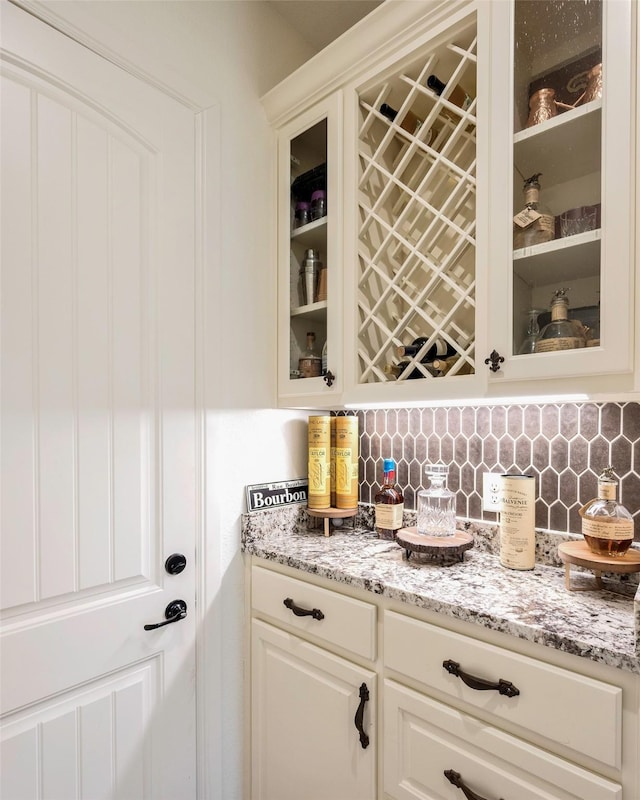 bar with decorative backsplash, white cabinetry, and light stone countertops