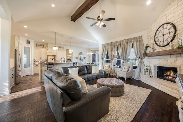 living room featuring ceiling fan with notable chandelier, dark wood-type flooring, beam ceiling, high vaulted ceiling, and a stone fireplace