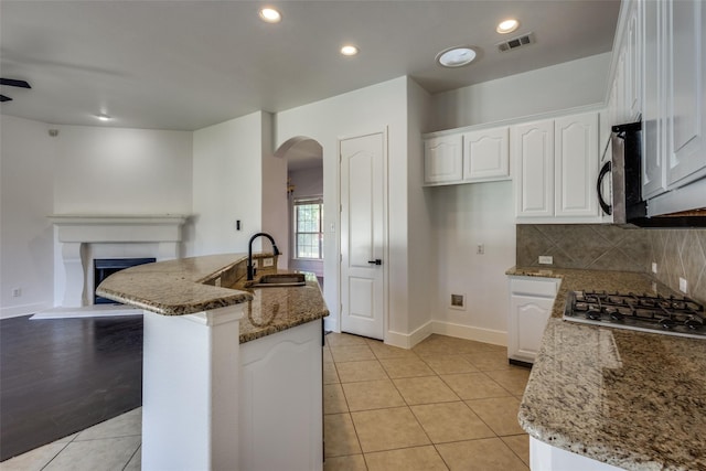 kitchen with backsplash, a kitchen island with sink, dark stone counters, sink, and white cabinetry