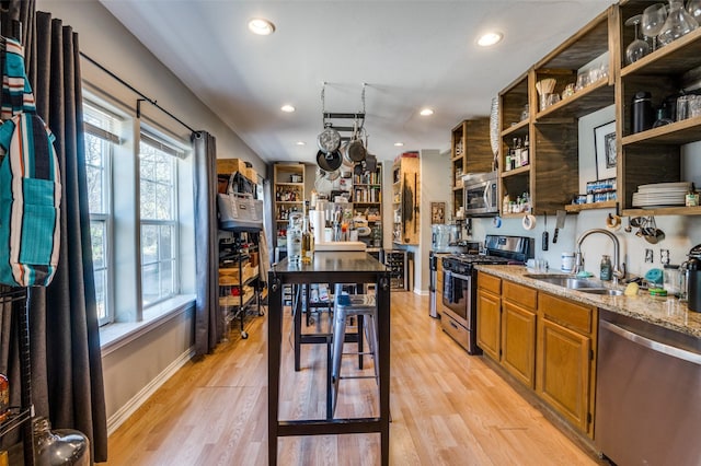 kitchen with light stone countertops, appliances with stainless steel finishes, light hardwood / wood-style floors, and sink