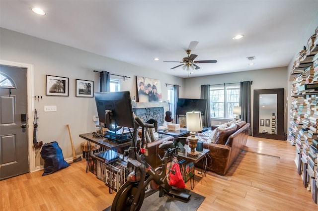 living room with ceiling fan, light wood-type flooring, and a stone fireplace