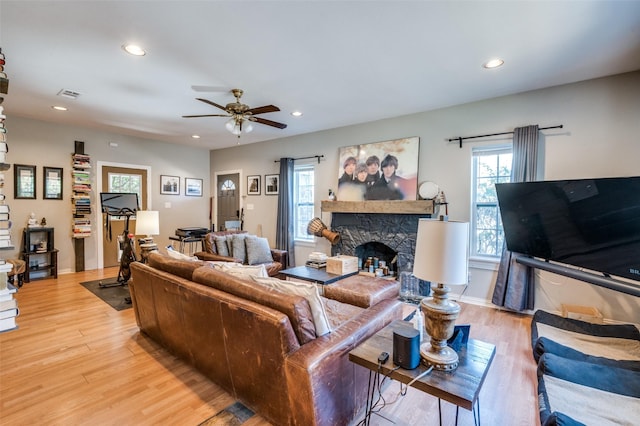 living room featuring ceiling fan, light wood-type flooring, and a stone fireplace