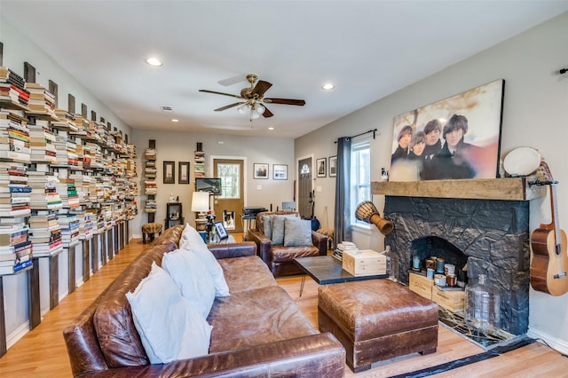 living room featuring ceiling fan, light hardwood / wood-style flooring, and a stone fireplace