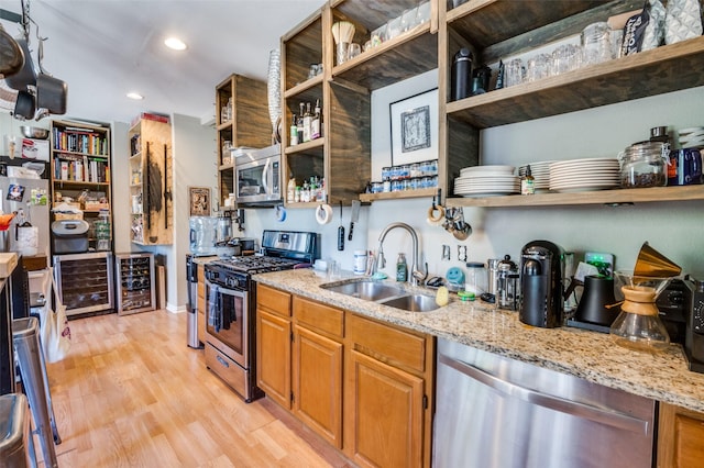 kitchen with wine cooler, stainless steel appliances, light stone counters, sink, and light hardwood / wood-style flooring