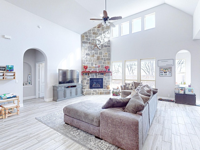 living room featuring high vaulted ceiling, a stone fireplace, ceiling fan, and light hardwood / wood-style flooring