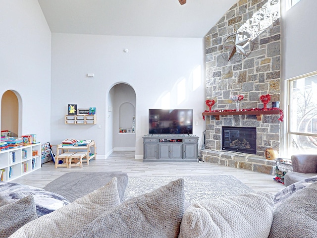 living room featuring light wood-type flooring, a stone fireplace, lofted ceiling, and plenty of natural light