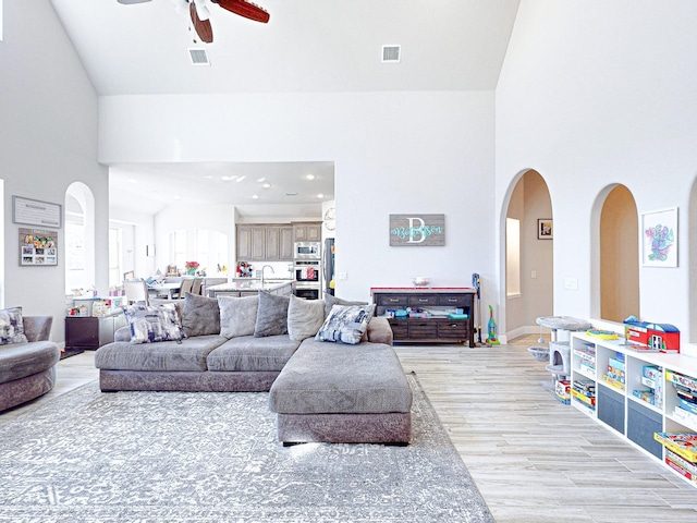 living room with light wood-type flooring, high vaulted ceiling, ceiling fan, and sink