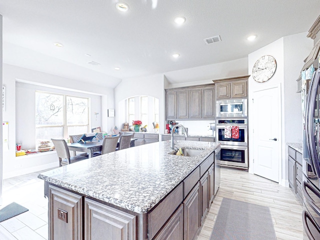 kitchen with light stone counters, stainless steel appliances, a center island with sink, and sink