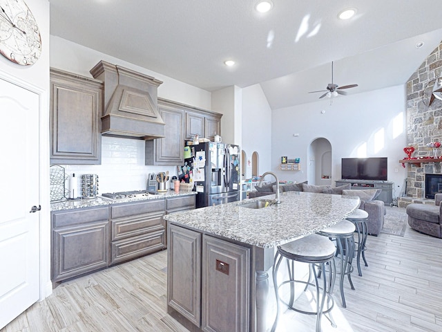 kitchen with custom exhaust hood, a kitchen island with sink, stainless steel appliances, sink, and backsplash