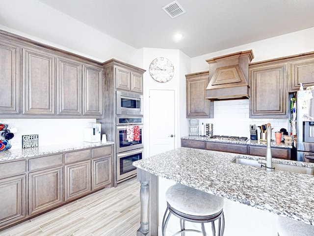 kitchen featuring a kitchen breakfast bar, custom exhaust hood, stainless steel appliances, light stone counters, and sink