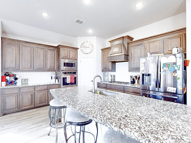 kitchen featuring light stone countertops, premium range hood, appliances with stainless steel finishes, and sink