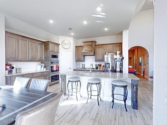 kitchen featuring stainless steel appliances, light wood-type flooring, light stone countertops, a kitchen bar, and sink