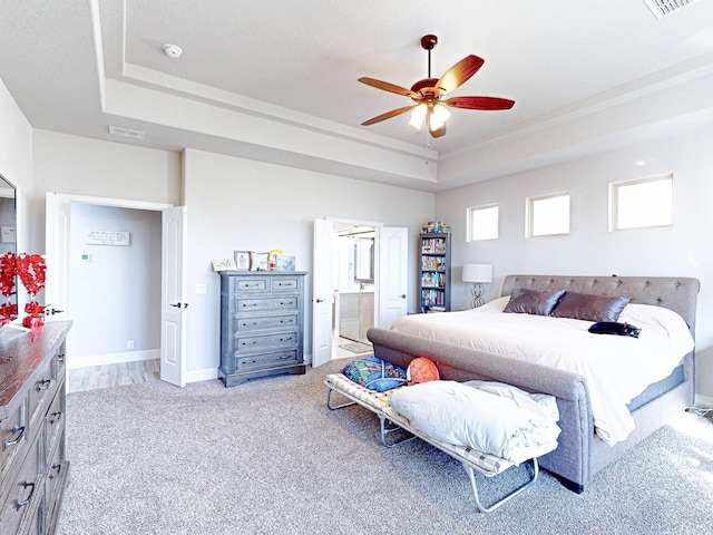 carpeted bedroom featuring ensuite bathroom, ceiling fan, and a tray ceiling