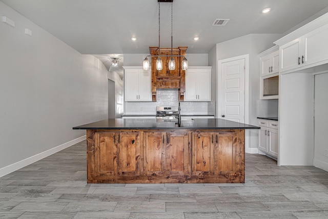 kitchen featuring decorative light fixtures, stainless steel range oven, white cabinetry, and a kitchen island with sink