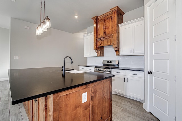 kitchen featuring sink, a center island with sink, white cabinets, stainless steel range with gas cooktop, and hanging light fixtures