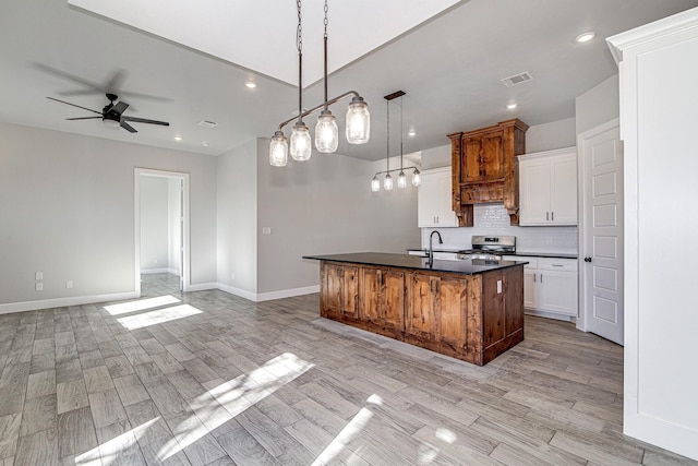 kitchen featuring light wood-type flooring, a kitchen island with sink, ceiling fan, pendant lighting, and white cabinetry