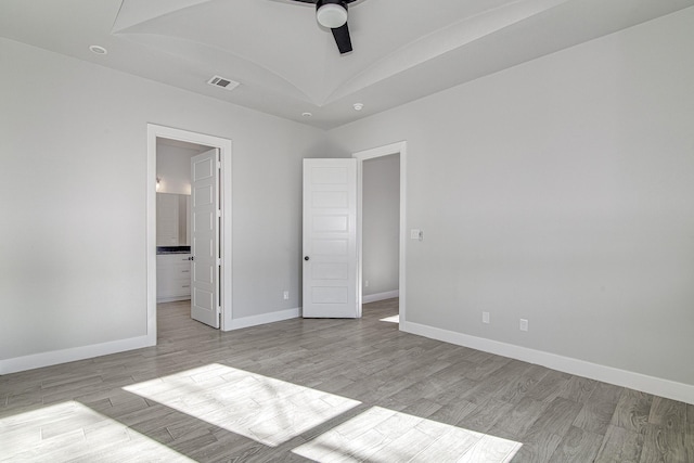 unfurnished bedroom featuring ceiling fan, light wood-type flooring, ensuite bathroom, and a tray ceiling