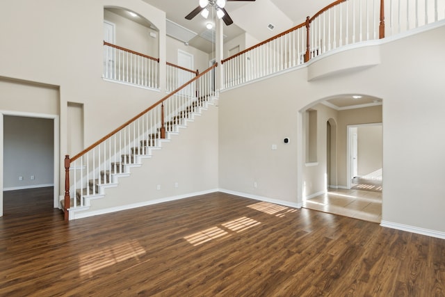 unfurnished living room featuring ceiling fan, dark hardwood / wood-style flooring, a towering ceiling, and ornamental molding